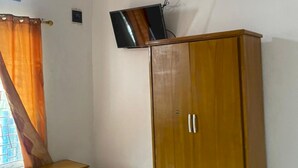 Een kamer met een houten garderobe, een klein houten tafeltje en een aan de muur bevestigde televisie.