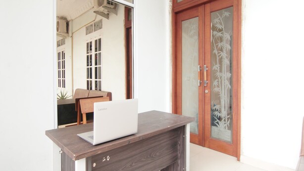 Een houten bureau met een laptop, een houten deur met glaspanelen, en een spiegelbeeld van een kamer met een stoel en een plant.