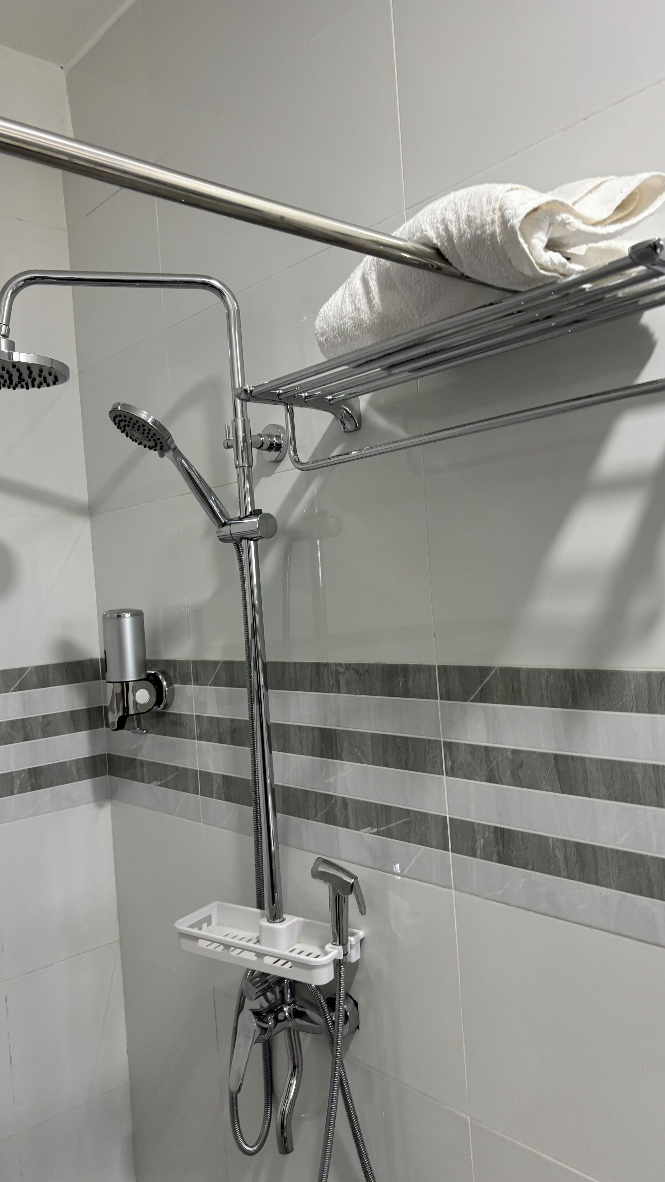 A shower area with a handheld showerhead, a wall-mounted faucet, and a handheld showerhead. There is a towel rack with a towel on it.