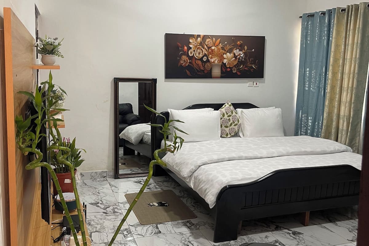 Une chambre à coucher avec un lit, un ventilateur de plafond, une plante en pot, un miroir et un tableau accroché au mur.