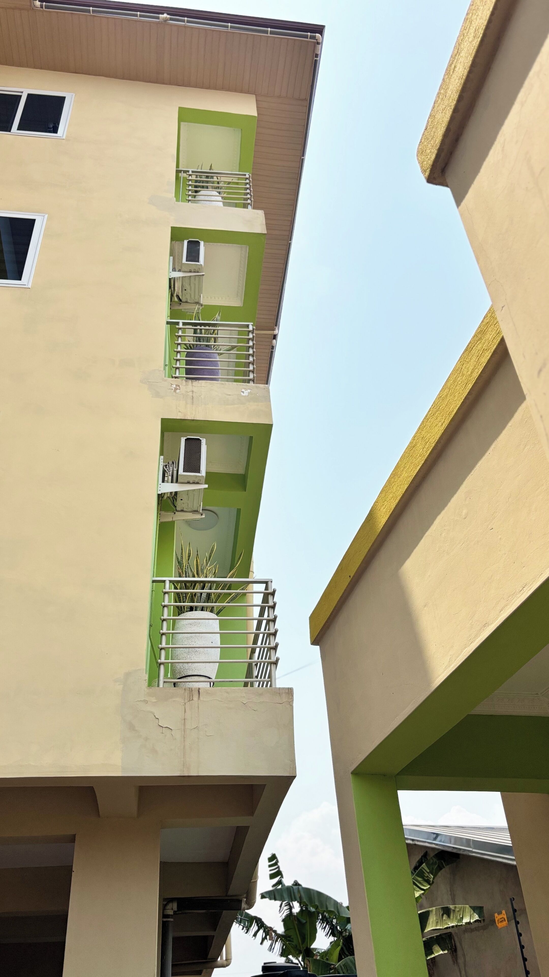 A multi-story building with balconies, air conditioning units, and a green and beige color scheme.