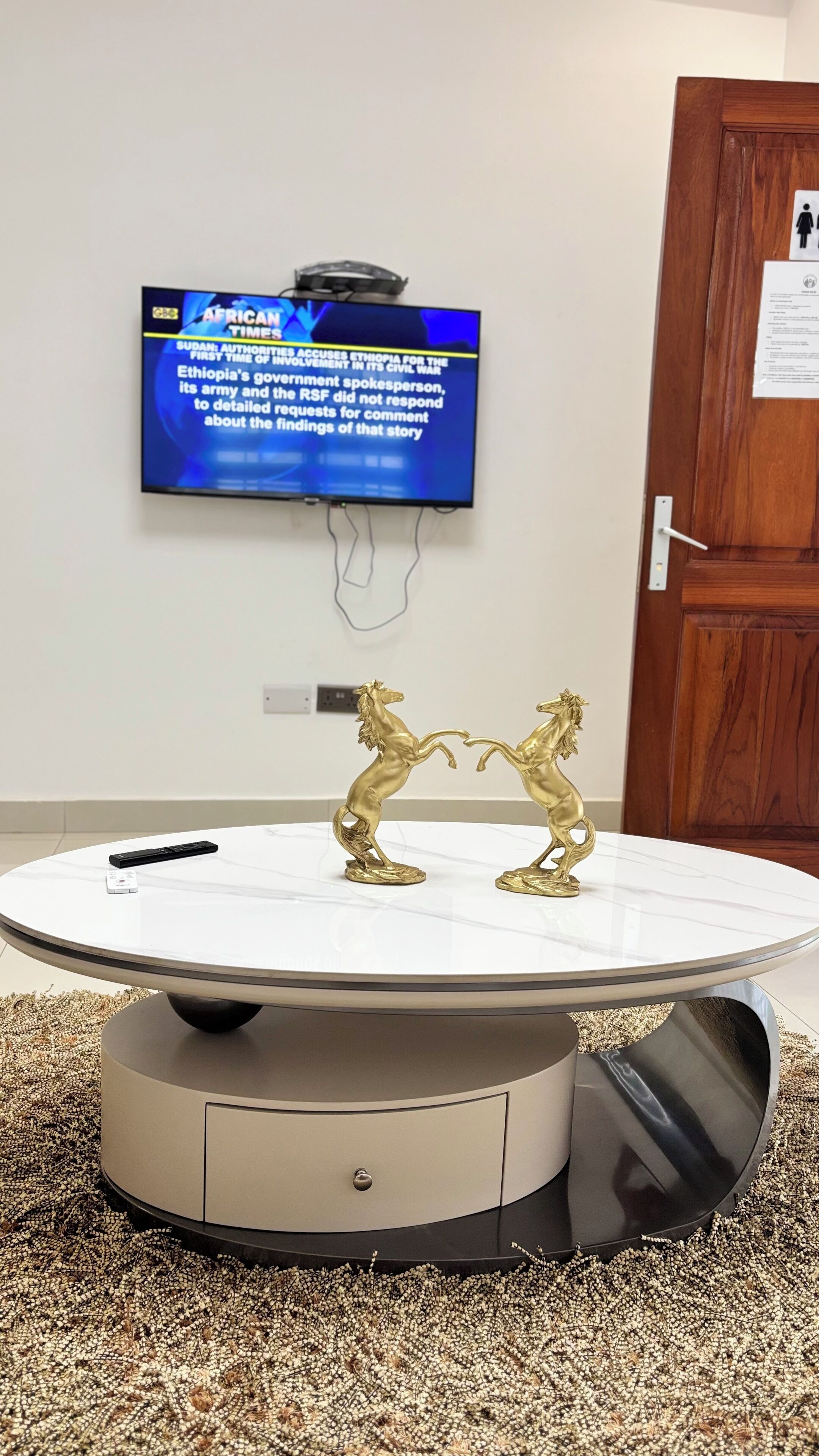 A round table with a white marble top, a remote control on it, and two golden horse statues.