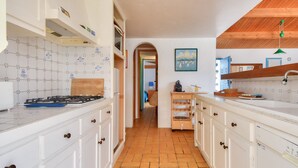 Una cocina con armarios blancos, salpicadero de azulejos, estufa a gas y techo de madera.