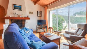 Un salón con chimenea, televisor y un ventanal con vistas a zonas verdes.