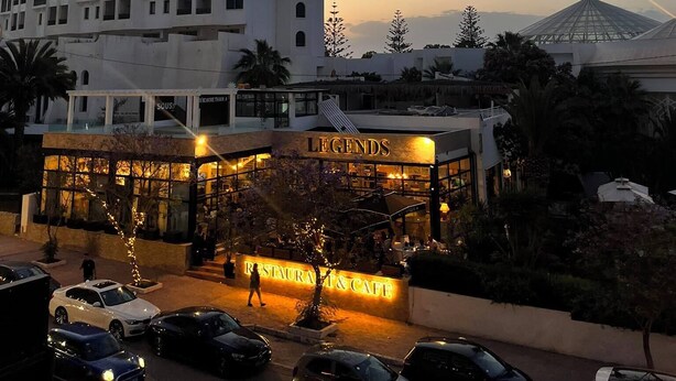 A hotel with a restaurant and cafe, a parking area, and a large building in the background. - The pearl of the Sousse tourist route 5 minutes from Boujaafer beach (Sousse)