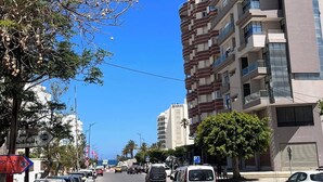 A street with parked cars, a multi-story building with balconies, and a clear blue sky. - The pearl of the Sousse tourist route 5 minutes from Boujaafer beach (Sousse)