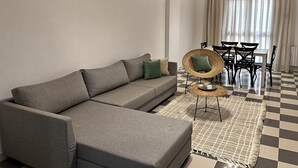 A modern living room with a grey sectional sofa, a woven chair, a dining table with chairs, and a checkered floor. - The pearl of the Sousse tourist route 5 minutes from Boujaafer beach (Sousse)