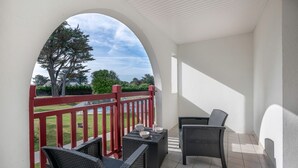 En balkon med fletningsmøbler, gelænder i rød farve og udsigt til træer og huse.
