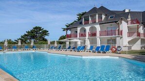 En swimmingpool med blå liggestole og en hvid bygning med altaner.