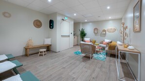 Et spa-rum med massagestole, en bænk, et siddeområde med stole, et lille bord og en plante.