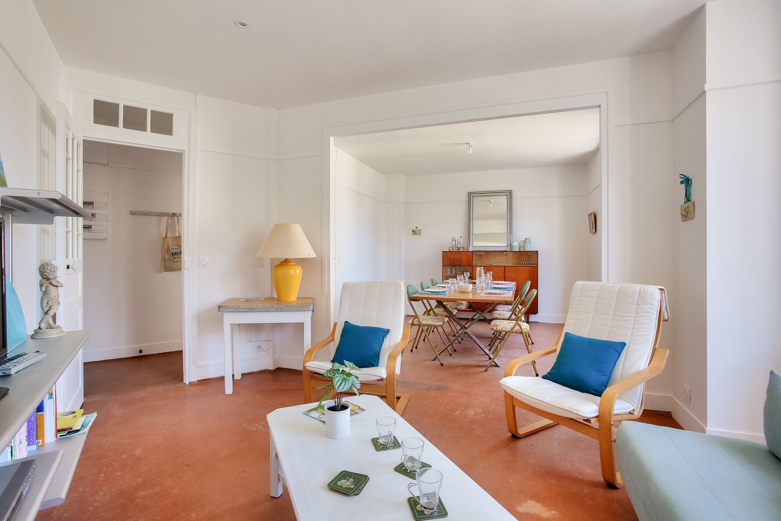 A spacious living room with a dining area, white walls, and a tiled floor.