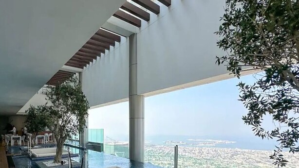 Une piscine à débordement moderne avec une bordure en verre, un espace salon et une vue sur la ville.