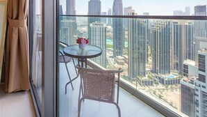 Un balcon avec une paroi en verre, une table ronde ornée d’un vase de fleurs et un fauteuil en osier.