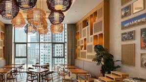 Un espace de restauration moderne avec des tables et des chaises rondes, des lampes suspendues en osier et une vue sur la ville grâce à de grandes fenêtres.