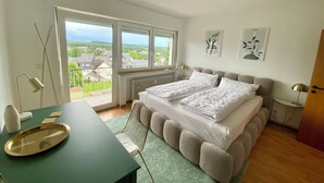 Ein Schlafzimmer mit großem Fenster, einem Bett, einem Schreibtisch und einem Stuhl.