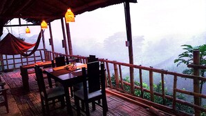 A covered outdoor seating area with tables and chairs, overlooking a mountainous landscape. - Cabañas arabi (Dosquebradas)