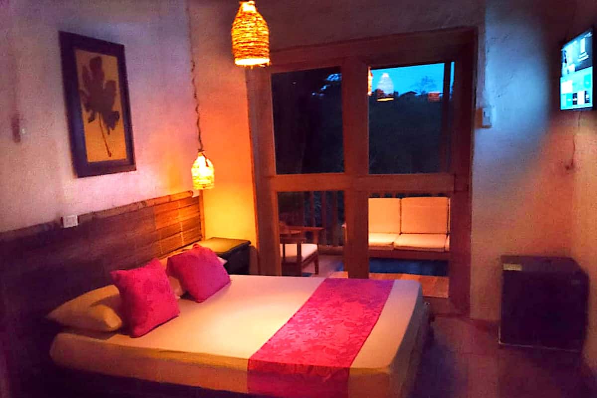A bedroom with a bed, pillows, a nightstand, a hanging light, a window, and a television.