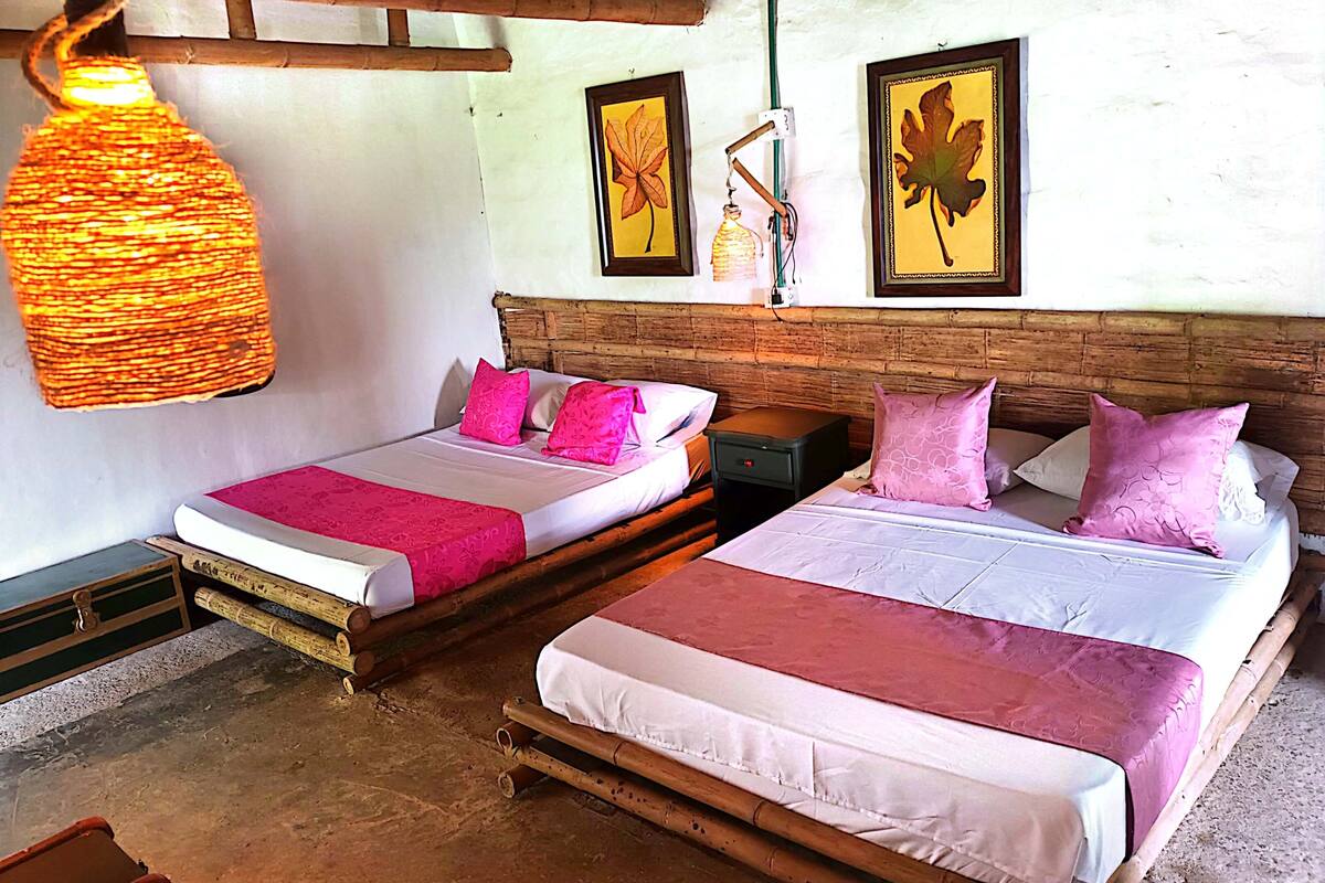 Two single beds with wooden frames and white bedding, pink pillows, and a hanging light fixture.