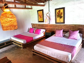 Two single beds with wooden frames and white bedding, pink pillows, and a hanging light fixture.