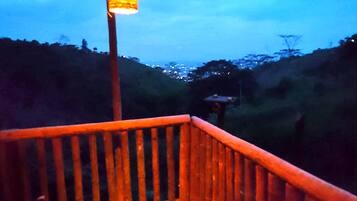 A wooden deck with a railing, a lantern, and a view of a cityscape in the background.