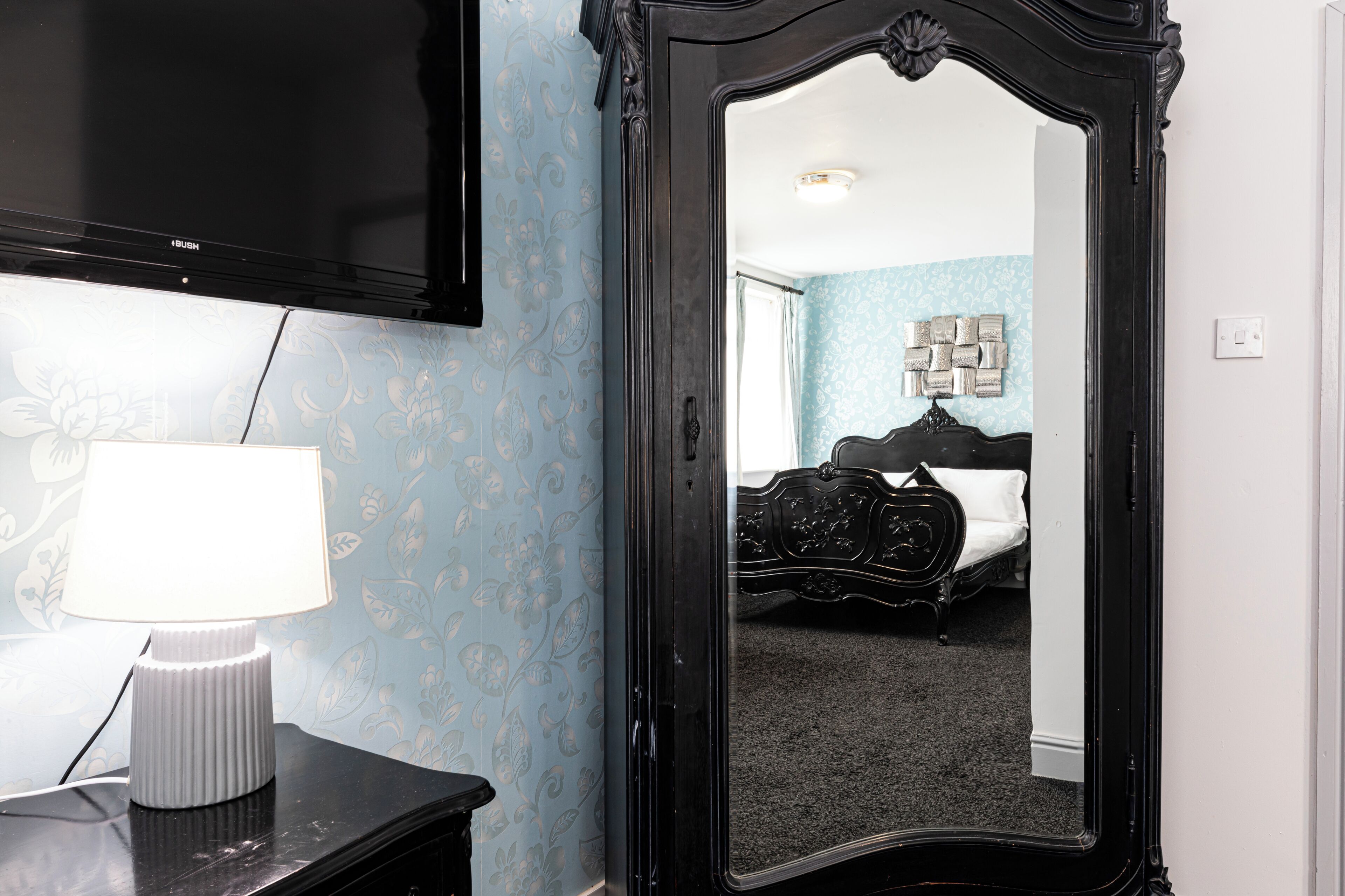 A room with a bed, a mirror, and a lamp on a dresser.