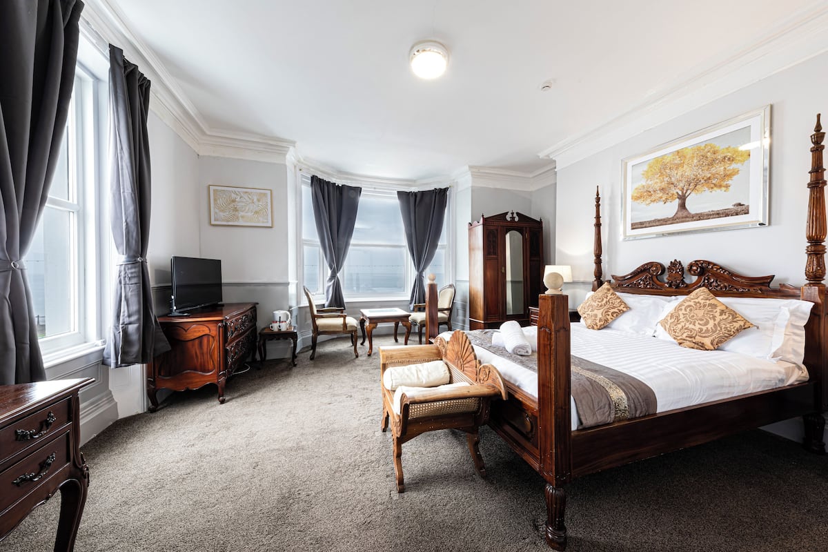 Quarto de hotel com uma cama grande, uma escrivaninha, uma cadeira, um armário e uma televisão.
