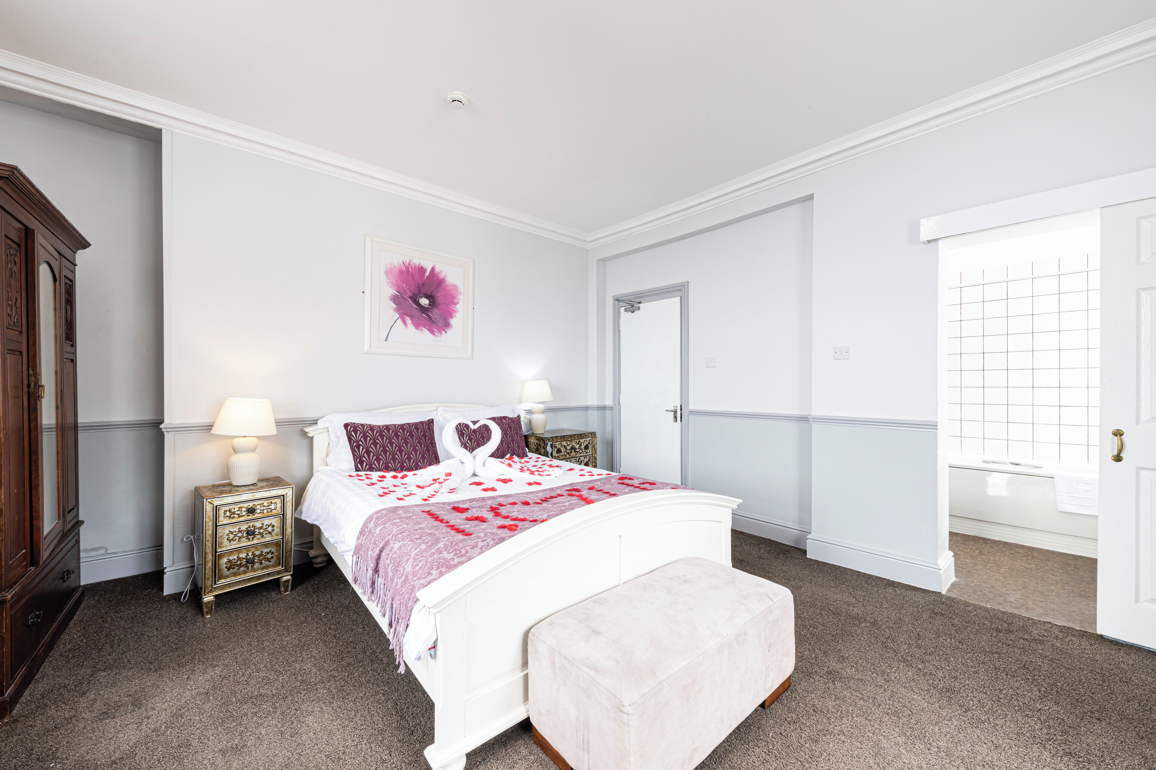 A bedroom with a white bed, a nightstand with a lamp, a decorative wall piece, and a door with a grid pattern.