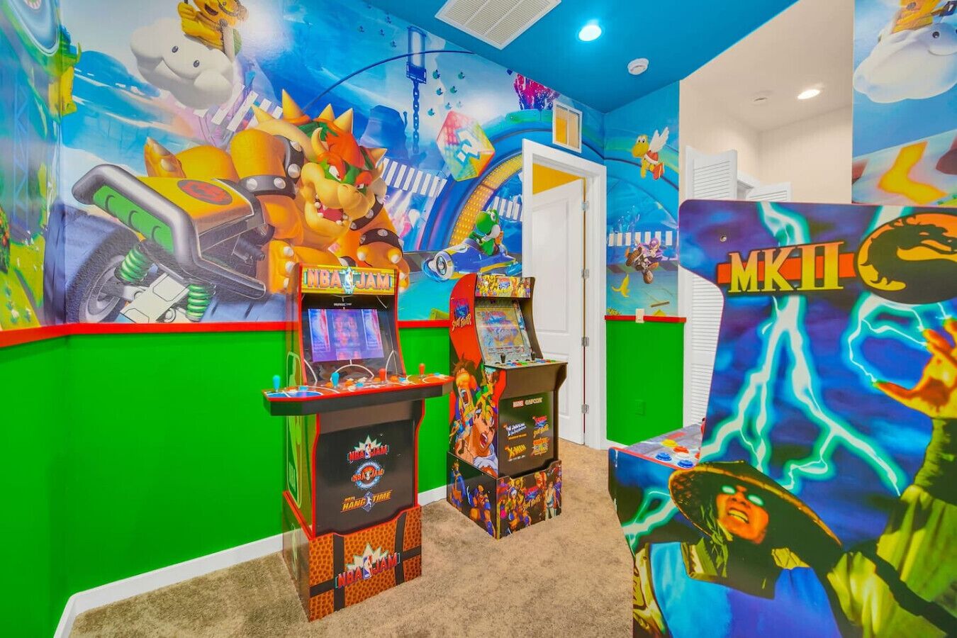 Una habitación con juegos de arcade, murales coloridos y una puerta que da a otra estancia.
