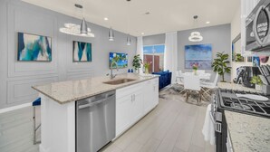 A modern kitchen with a central island, stainless steel appliances, pendant lighting, and artwork on the walls. - 3BD/3BA Themed House Near Disney (Kissimmee)