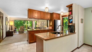 A spacious kitchen with wooden cabinets, a granite countertop, and a refrigerator. - Kauai Waikomo Stream Villas by Coldwell Banker Island Vacations (Koloa)