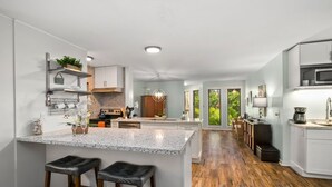 A modern kitchen with a central island, wooden flooring, and a view of the outdoors. - Kauai Waikomo Stream Villas by Coldwell Banker Island Vacations (Koloa)