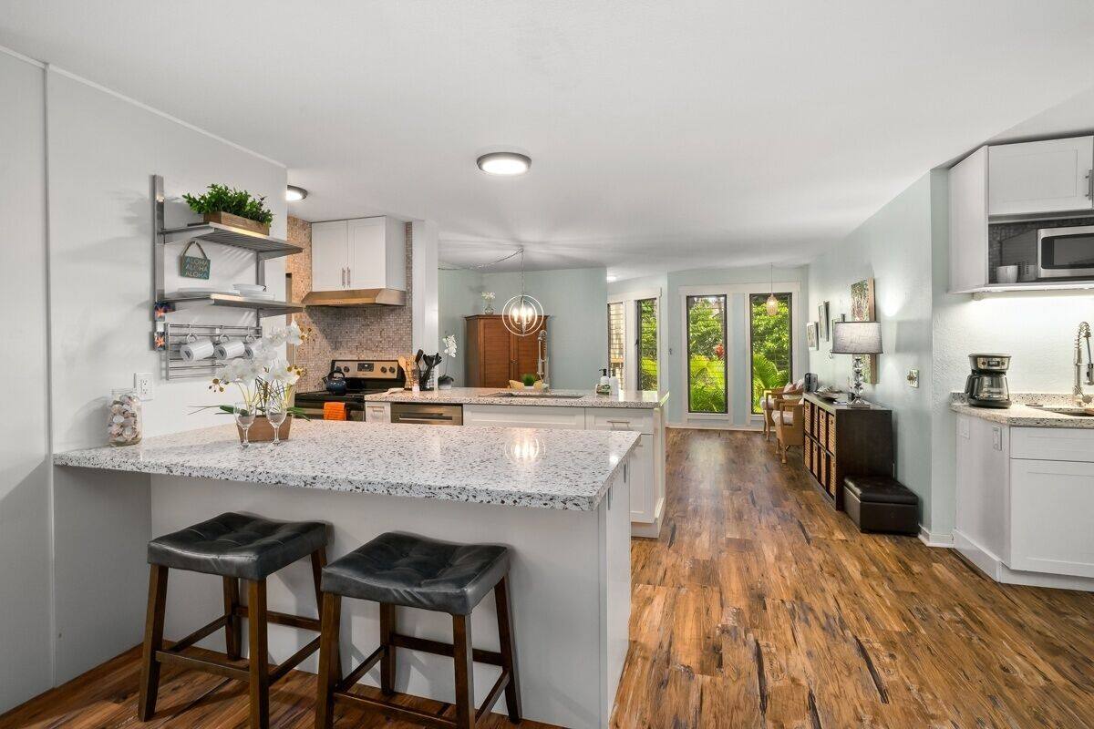 A modern kitchen with a central island, wooden flooring, and a view of the outdoors.