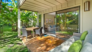 A patio with a table and chairs, a sofa, and a glass door leading to a garden. - Kauai Waikomo Stream Villas by Coldwell Banker Island Vacations (Koloa)