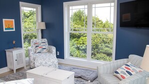 A room with a large window, a white chair with starfish pattern, a striped sofa, and a television mounted on the wall. - Hot Mess - Pool, Oceanview, Pet-Friendly Home (Emerald Isle)