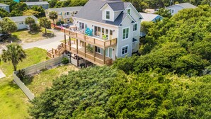 A two-story house with a balcony, surrounded by lush greenery and a view of the sea. - Hot Mess - Pool, Oceanview, Pet-Friendly Home (Emerald Isle)