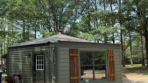 Una cabaña pequeña de un piso con techo de metal, puerta corredera de vidrio y contraventanas de madera.