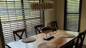 Un comedor con una mesa de madera, seis sillas, individuales tejidas y una lámpara colgante.