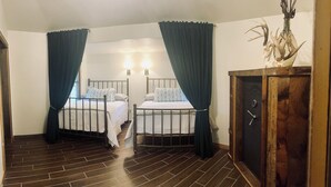 Una habitación con dos camas, cortinas oscuras, un armario de madera y un jarrón decorativo con cuernos.