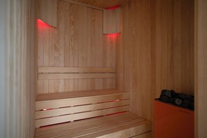 Relax in a cozy sauna with a heat source and wooden bench.