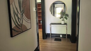 A hallway with a framed artwork, a round mirror, and a small table with a plant.