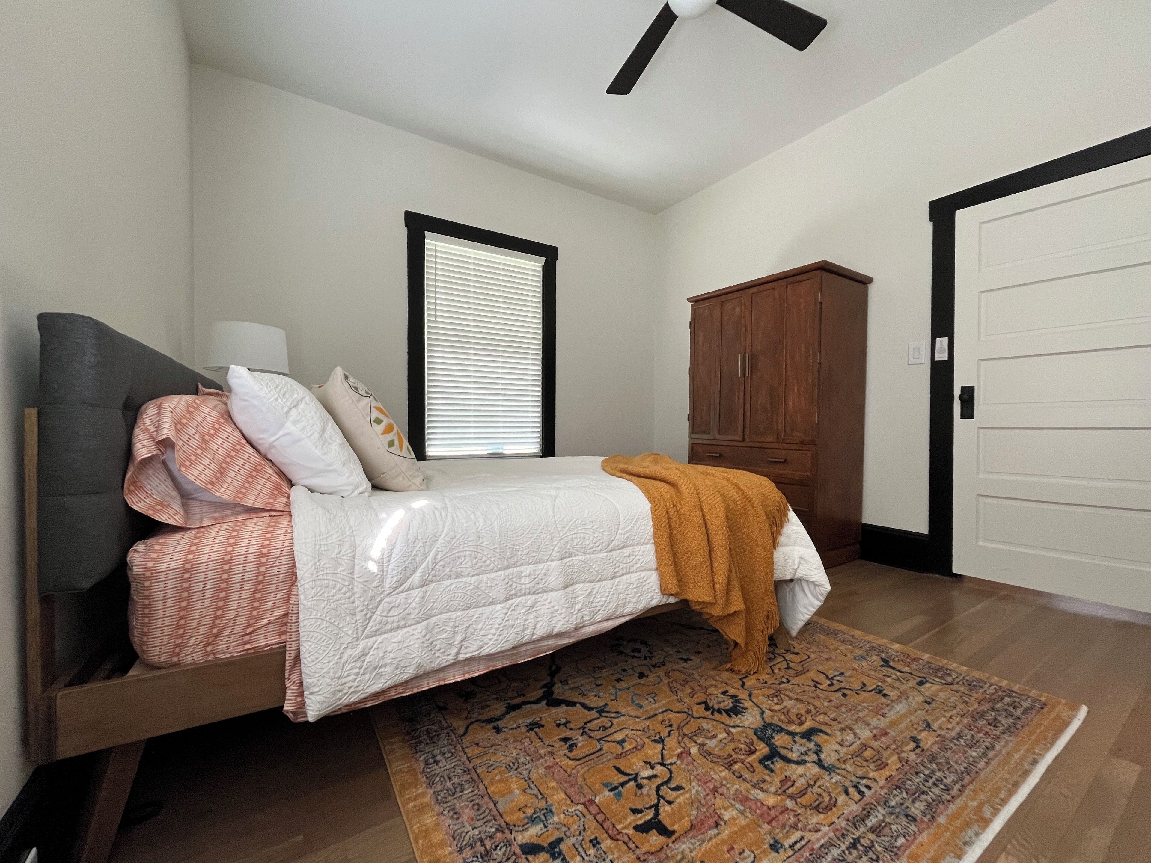 A bedroom with a bed, a nightstand, a wardrobe, a window with blinds, and a ceiling fan.