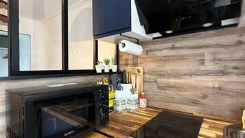 Une cuisine moderne avec un micro-ondes noir, un plan de travail en bois et une cuisinière intégrée.