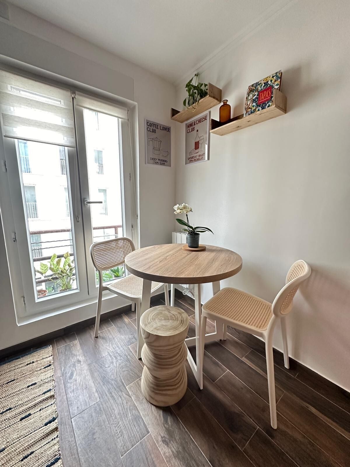 Un coin repas avec une table ronde en bois, deux chaises blanches et une petite plante en pot.