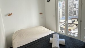 A bedroom with a bed, a ceiling fan, a clock, and a window with a view of buildings. - Modern cozy studio near Montmartre, 2min walk to metro Château Rouge (Paris)