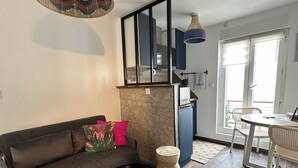 A modern living room with a dark sofa, a round black coffee table, and a colorful rug. A large woven light fixture hangs from the ceiling, and a dining area with a table and chairs is visible in the background. - Modern cozy studio near Montmartre, 2min walk to metro Château Rouge (Paris)