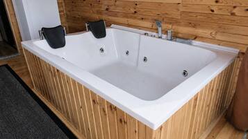 Jacuzzi rectangular con dos toallas negras, paneles de madera en las paredes y un tapete con estampado blanco y negro.
