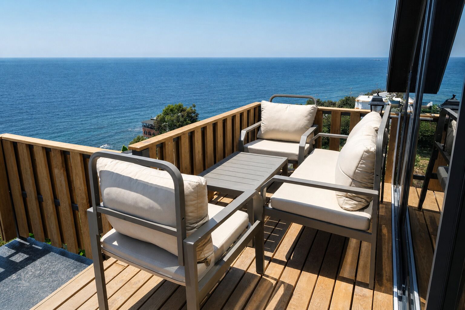 An outdoor seating area with a view of the sea, wooden deck flooring, and metal-framed chairs.