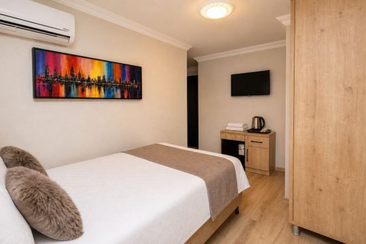 Una habitación de hotel con cama, un cuadro, un televisor y una kitchenette.