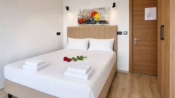A neatly made bed with white linens, a single red rose, and two folded towels.
