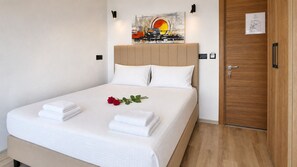 A neatly made bed with white linens, a single red rose, and two folded towels.